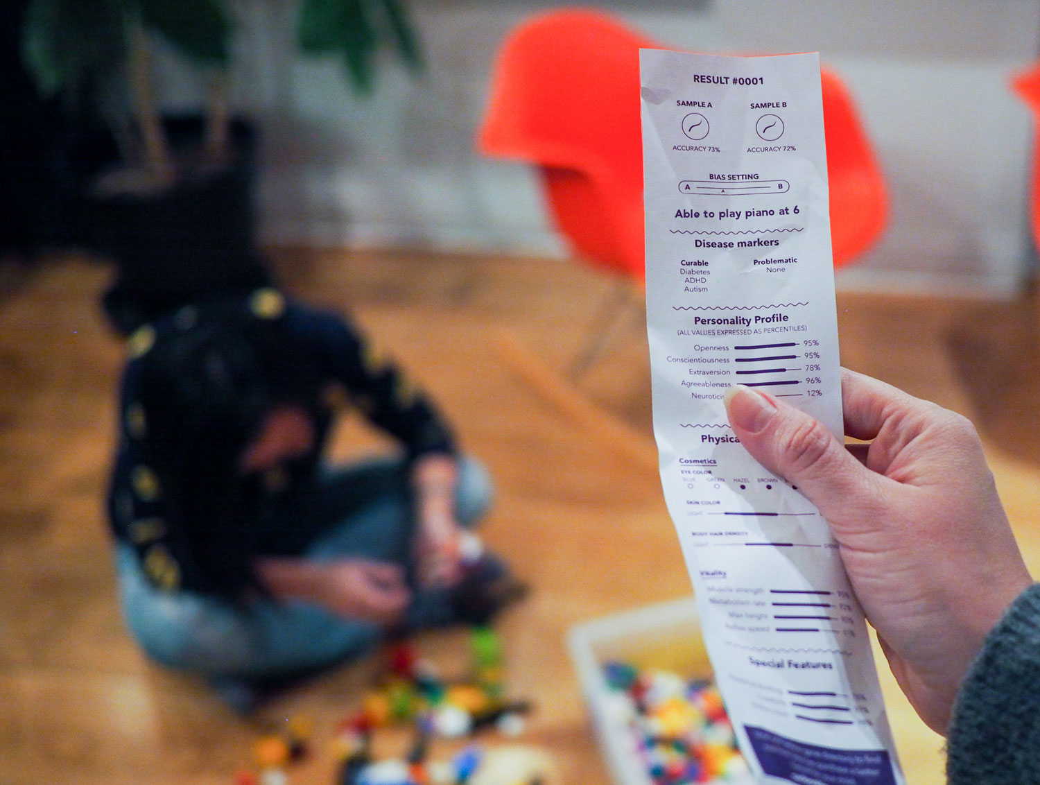 A person holds a printout from the Combinator showing that the child would be above average, while looking at a child playing legos